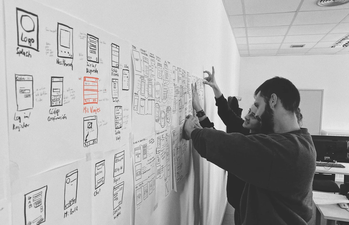 Two people arranging a wall of hand-drawn application screens into one system