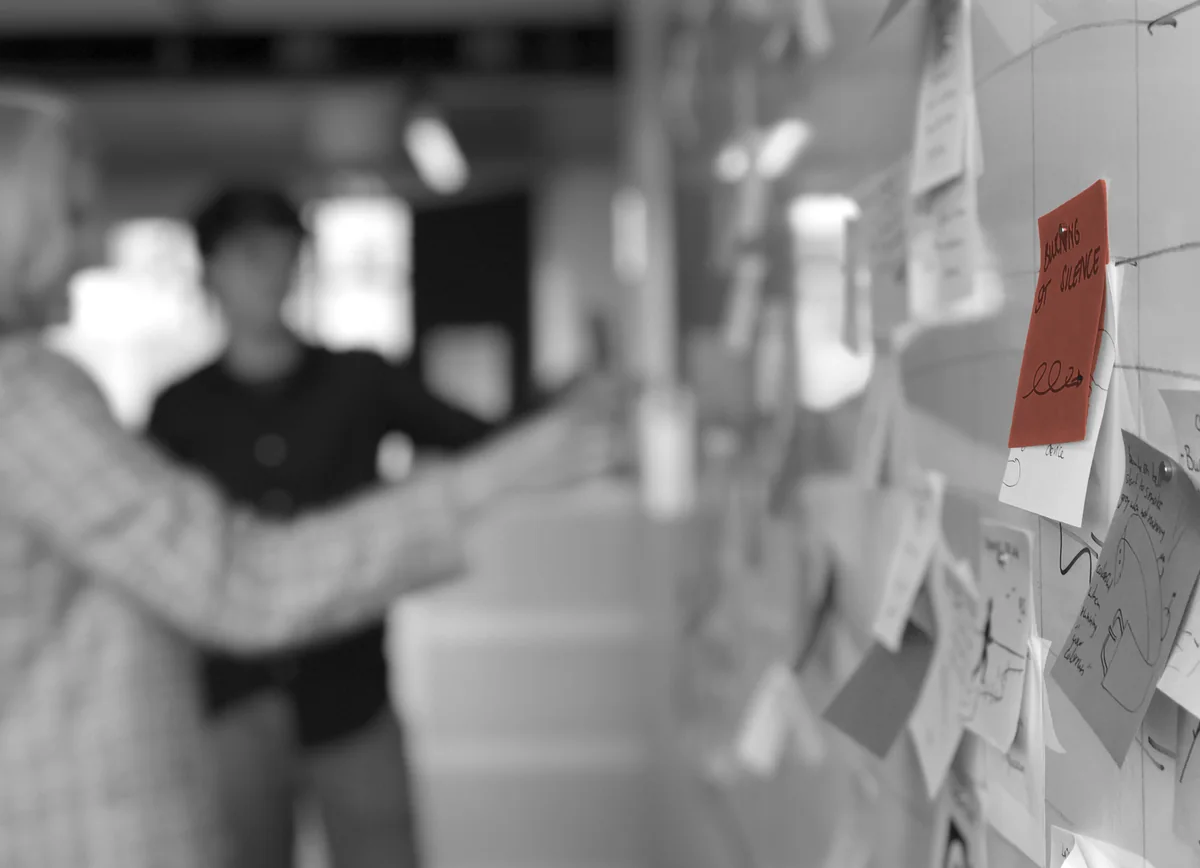Written notes on a glass wall, one picked out in colour, with colleagues talking behind it